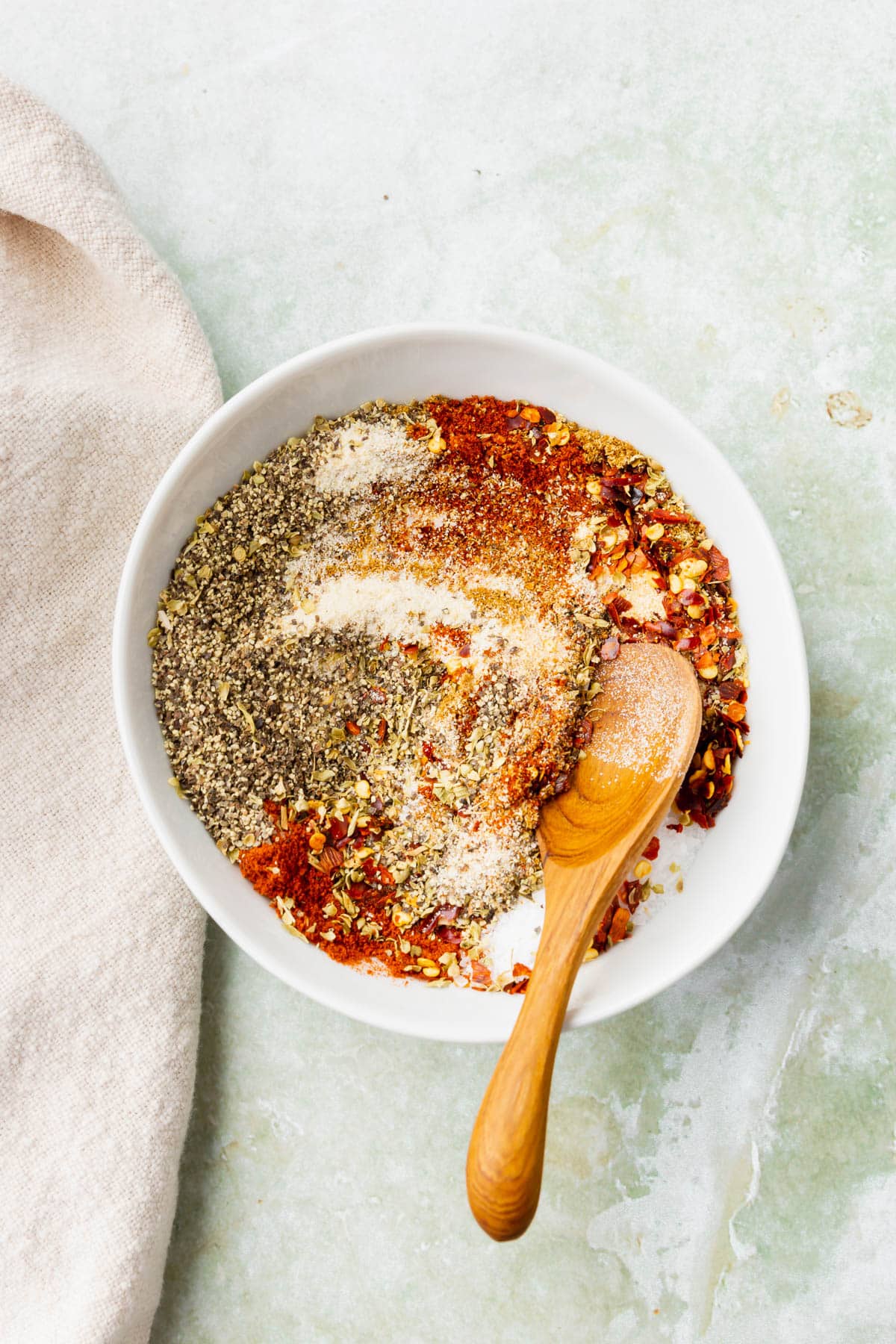 Spices in a white bowl being mixed up with a wooden spoon to make a gluten-free taco seasoning blend.