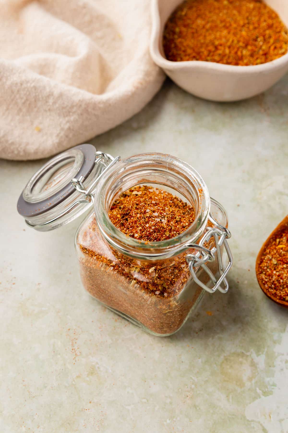 Gluten-free taco seasoning in a glass jar on a green marble table with a bowl of spice blend in the background.