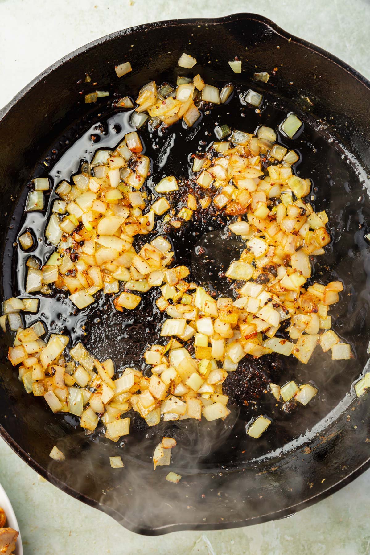 A large cast irion skillet with diced onions and garlic that have been sautéed in olive oil.