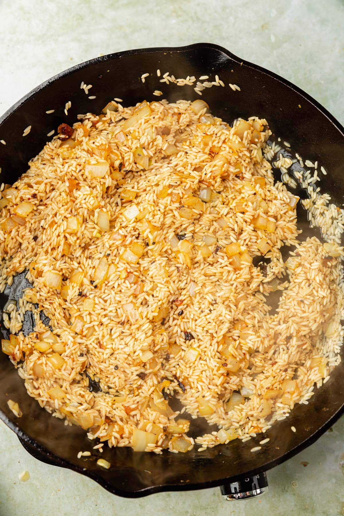 A large cast iron skillet with uncooked rice and sautéed onions in it mixed with white wine.