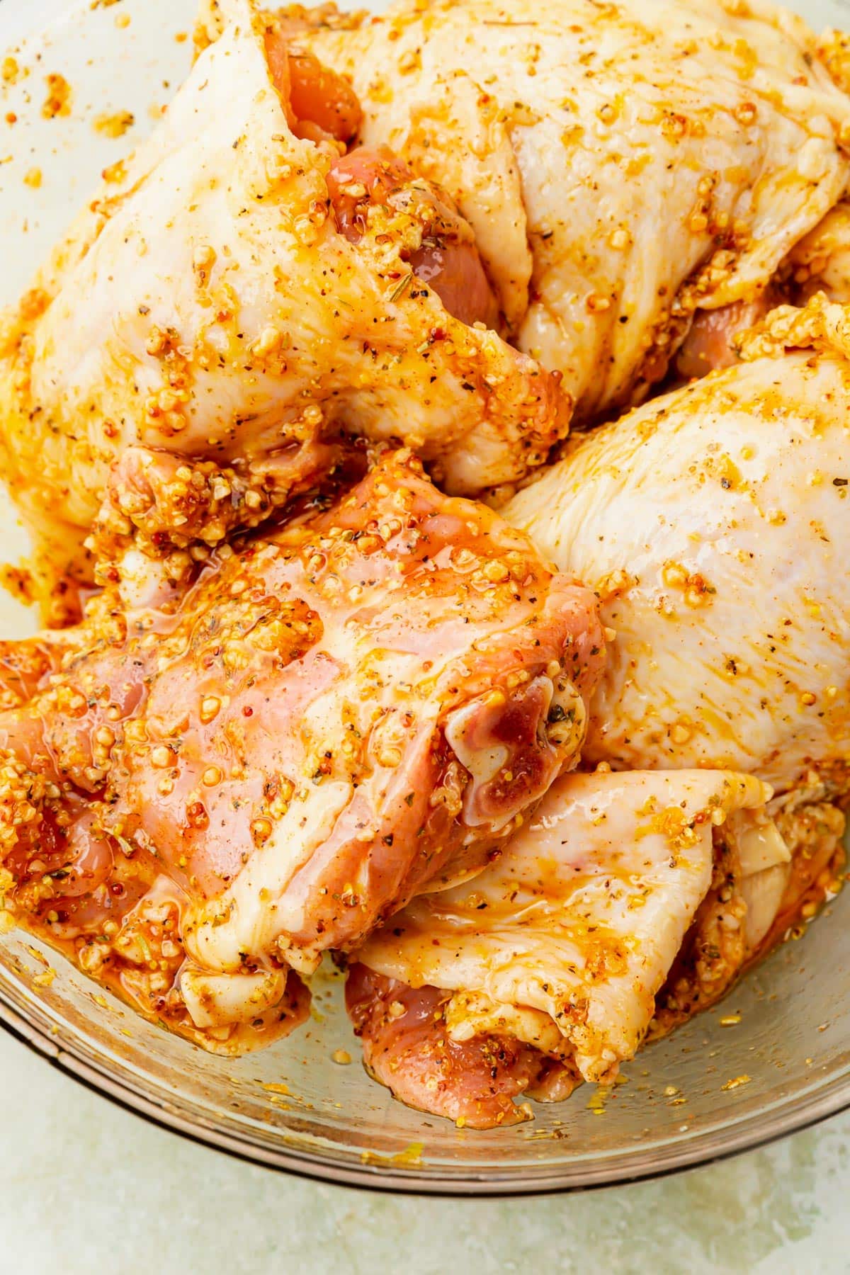 A glass mixing bowl of raw chicken thighs tossed in a garlic lemon marinade.