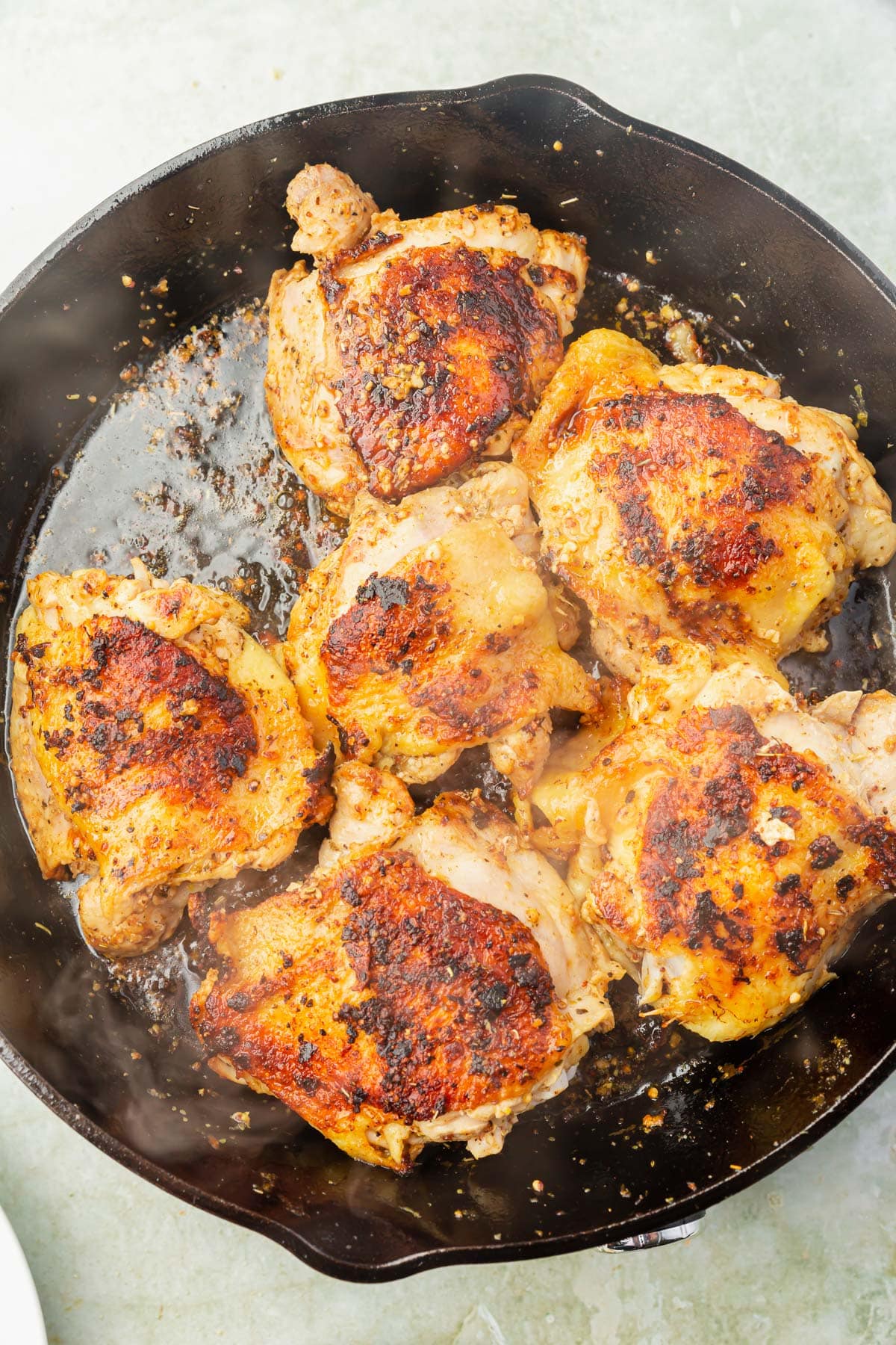 A large cast iron skillet with browned chicken thighs in it.