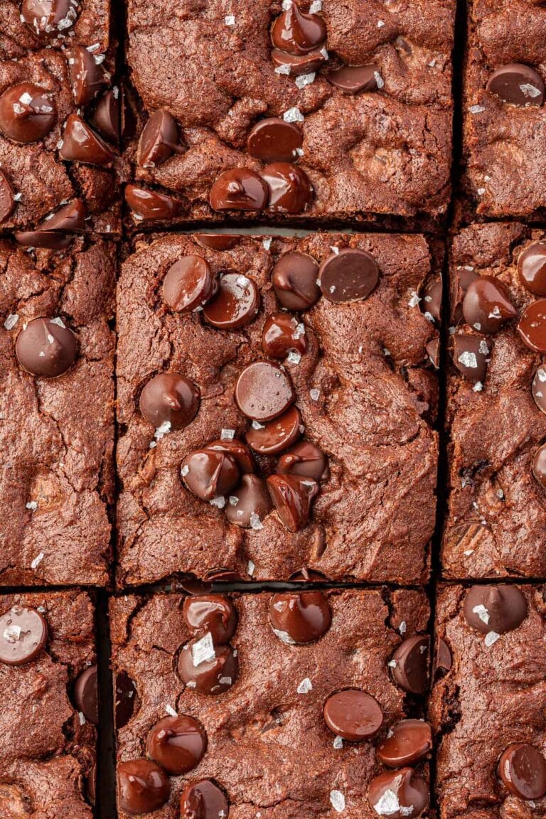 An overhead view of gluten-free brownies cut into 9 equal pieces and topped with semi-sweet chocolate chips and flaky sea salt.