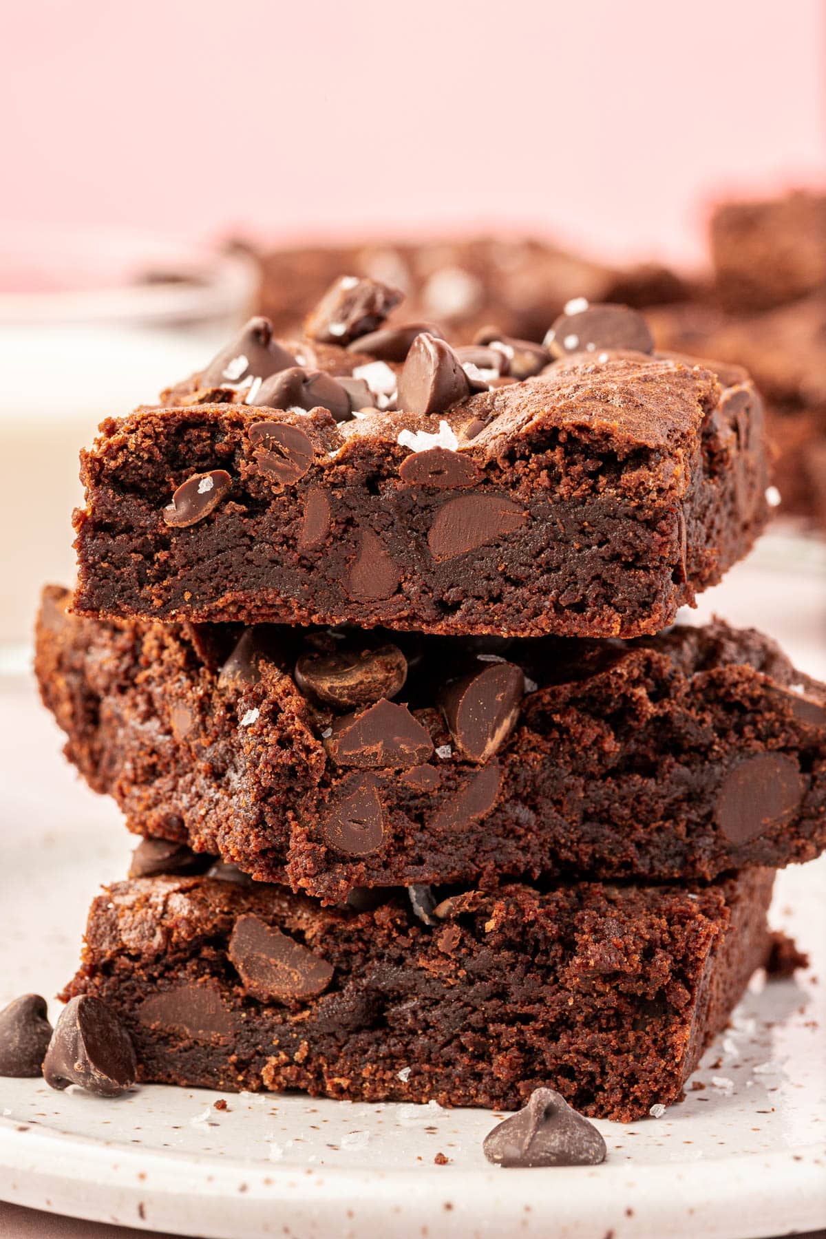 A stack of three gluten-free brownies on a small dessert plate topped with semi-sweet chocolate chips and flaky sea salt.