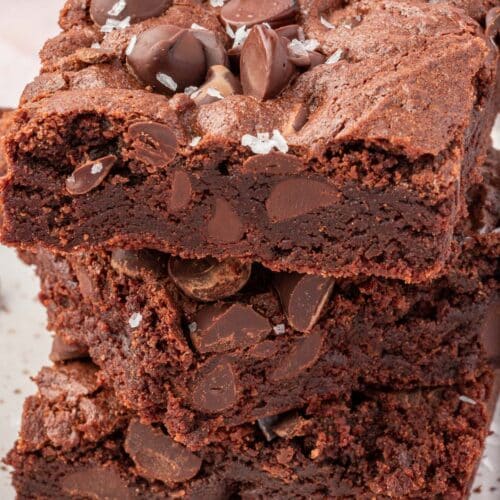 A stack of three gluten-free brownies topped with semi-sweet chocolate chips and flaky sea salt.