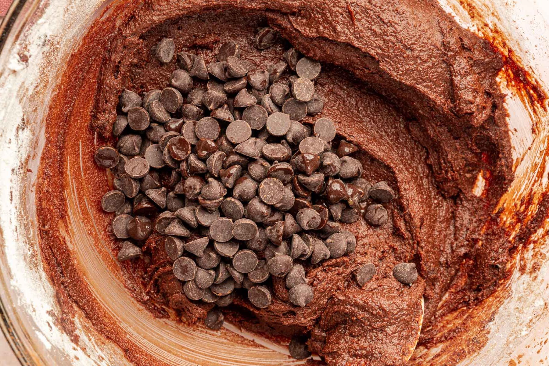 A closeup of gluten-free batter in a mixing bowl topped with a pile of semi-sweet chocolate chips.