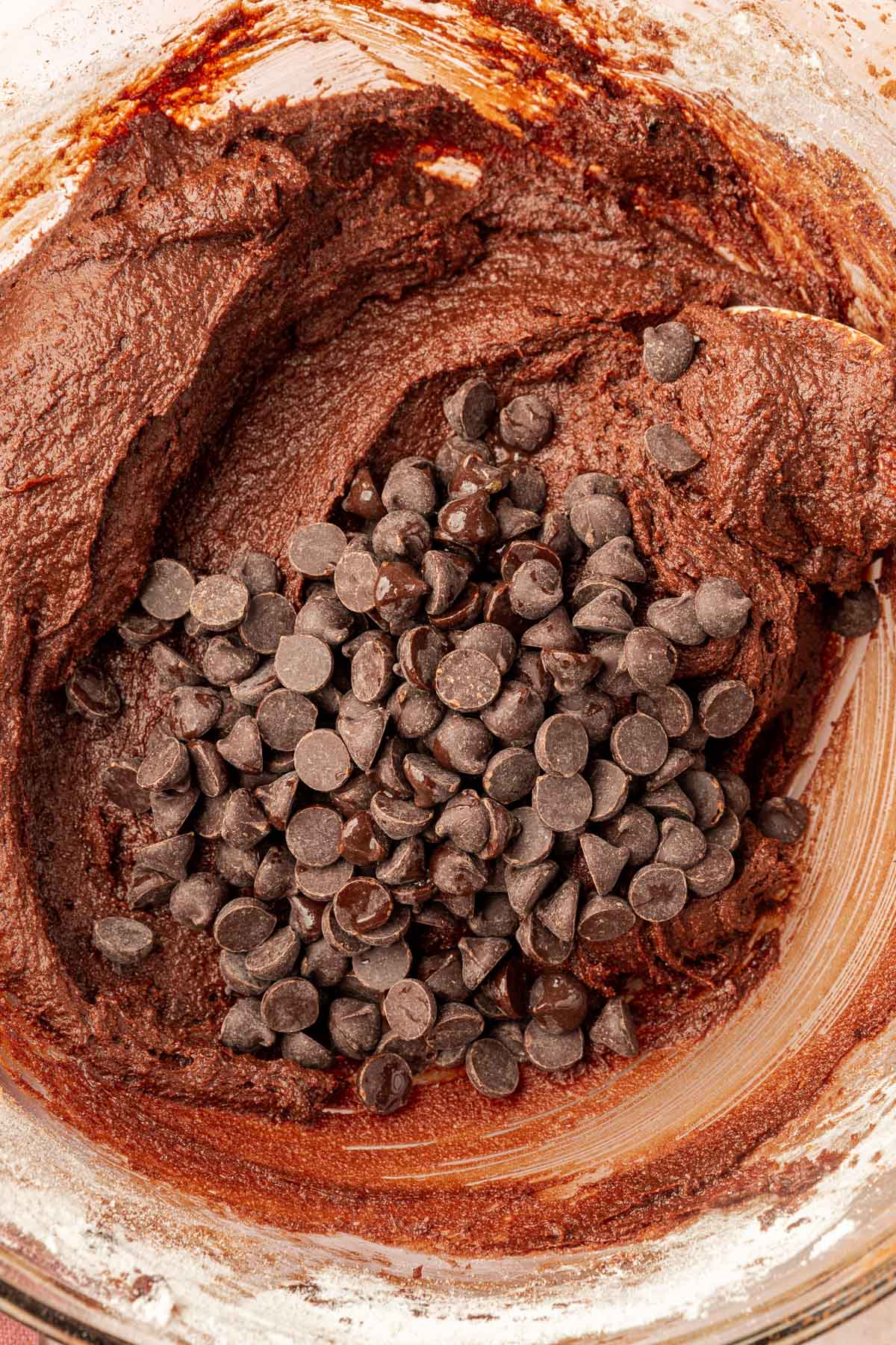A closeup of gluten-free batter in a mixing bowl topped with a pile of semi-sweet chocolate chips.