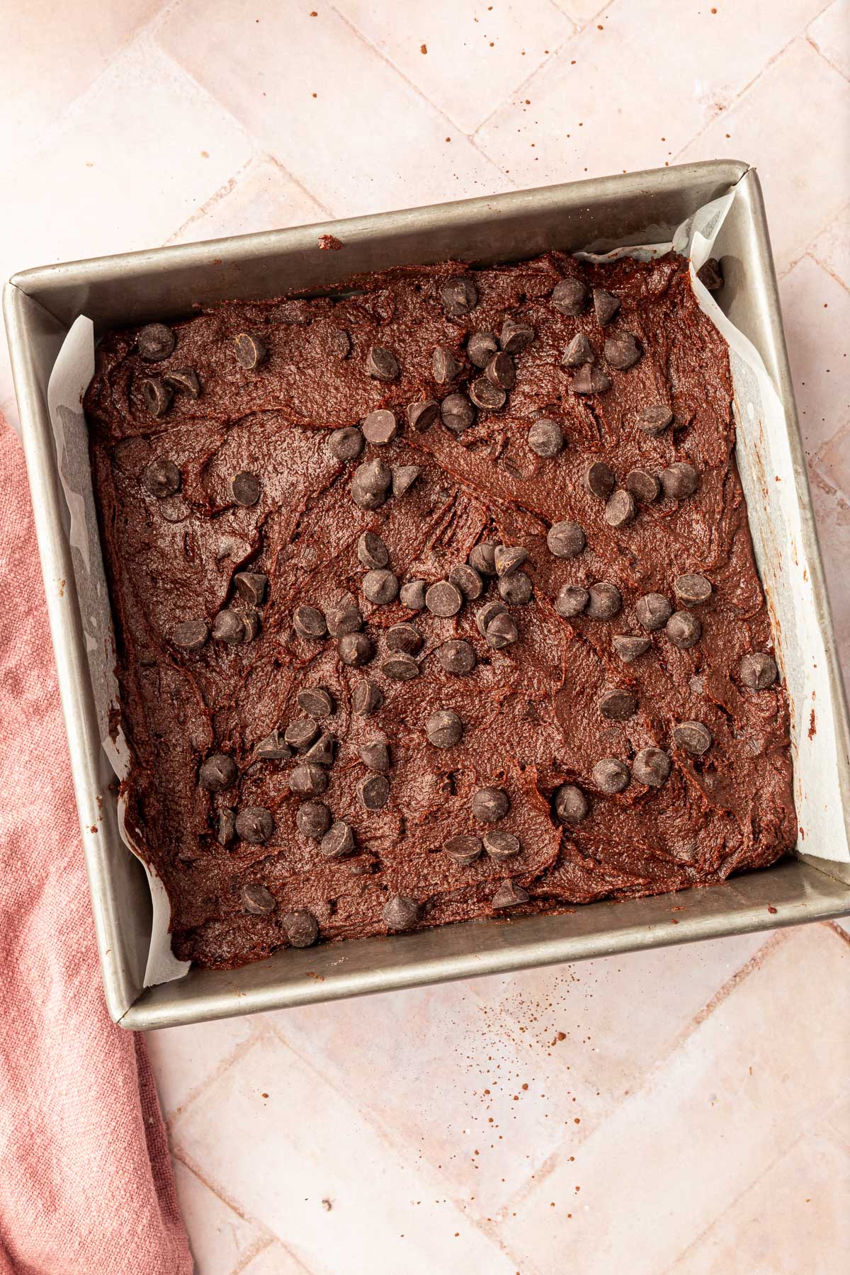 A square baking pan filled with brownie batter and topped with semi-sweet chocolate chips before baking in the oven.