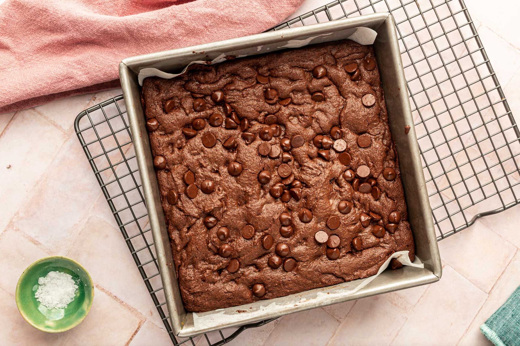 A square baking pan filled with baked gluten-free brownies on top of a pink background.
