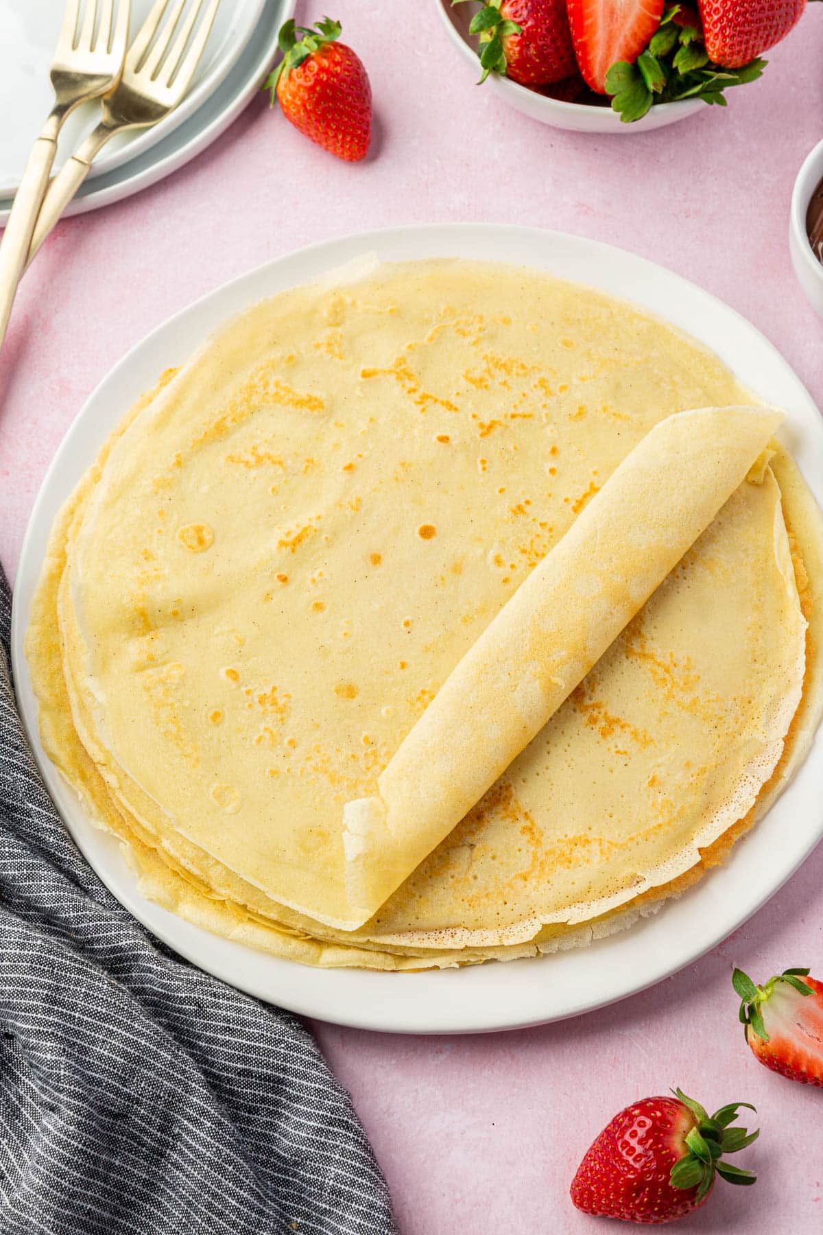 A stack of gluten-free crepes on a plate with the top one halfway rolled into a cyllinder.