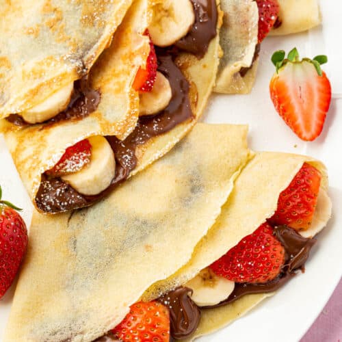 A closeup of two gluten-free crepes filled with nutella, sliced strawberries, and banana slices.