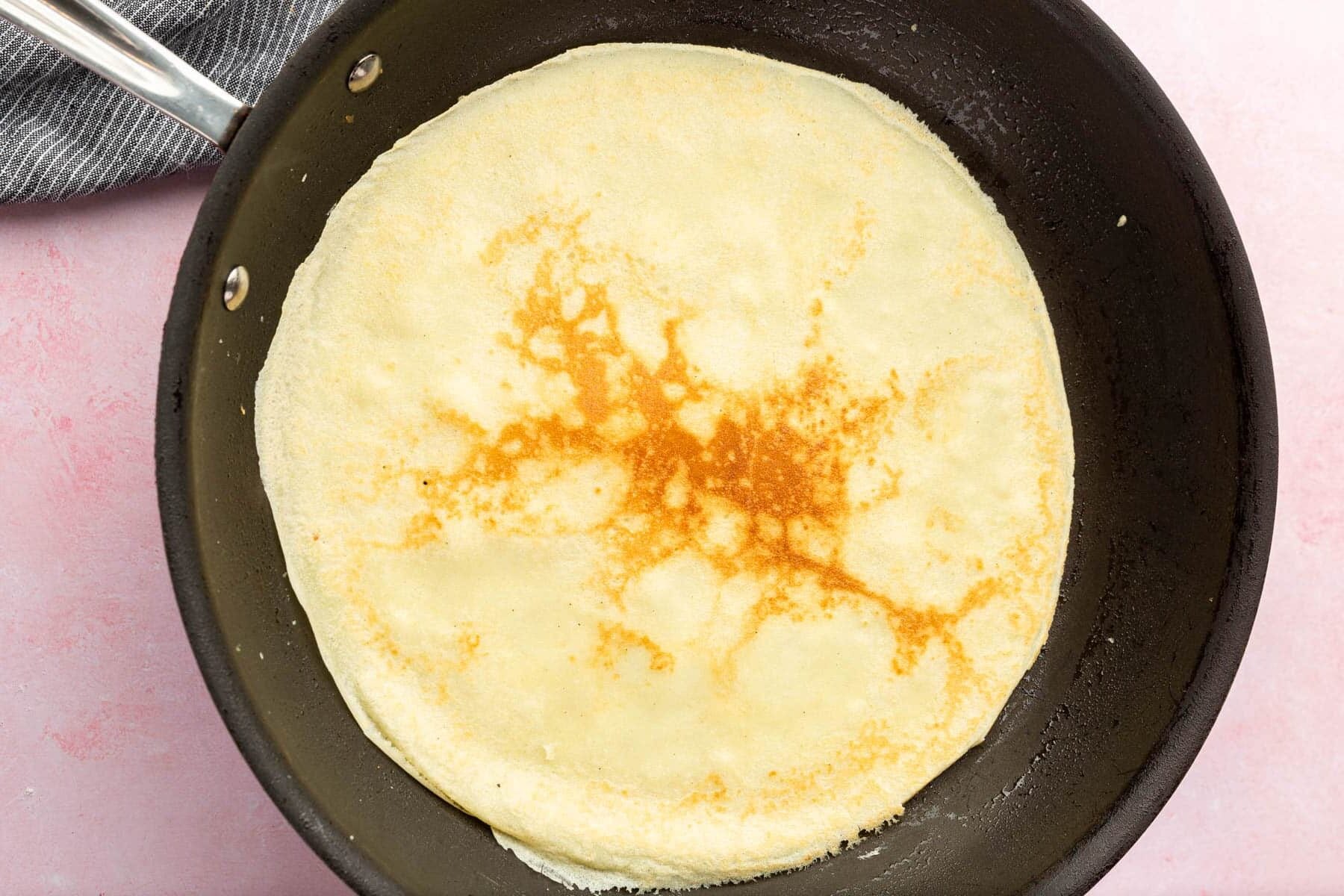 A gluten-free crepe cooking in a non-stick skillet.