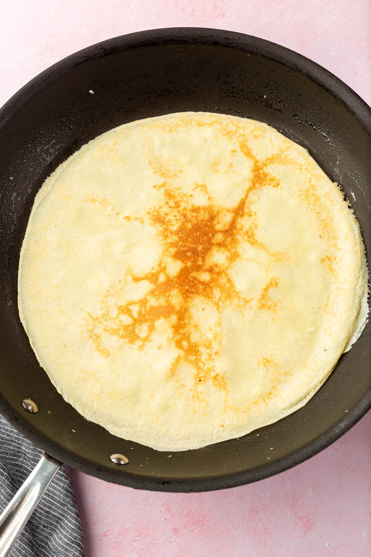 A gluten-free crepe cooking in a non-stick skillet.