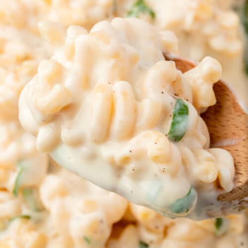 A closeup of a wooden spoon with a big scoop of mozzarella mac and cheese over a large skillet of mac and cheese.