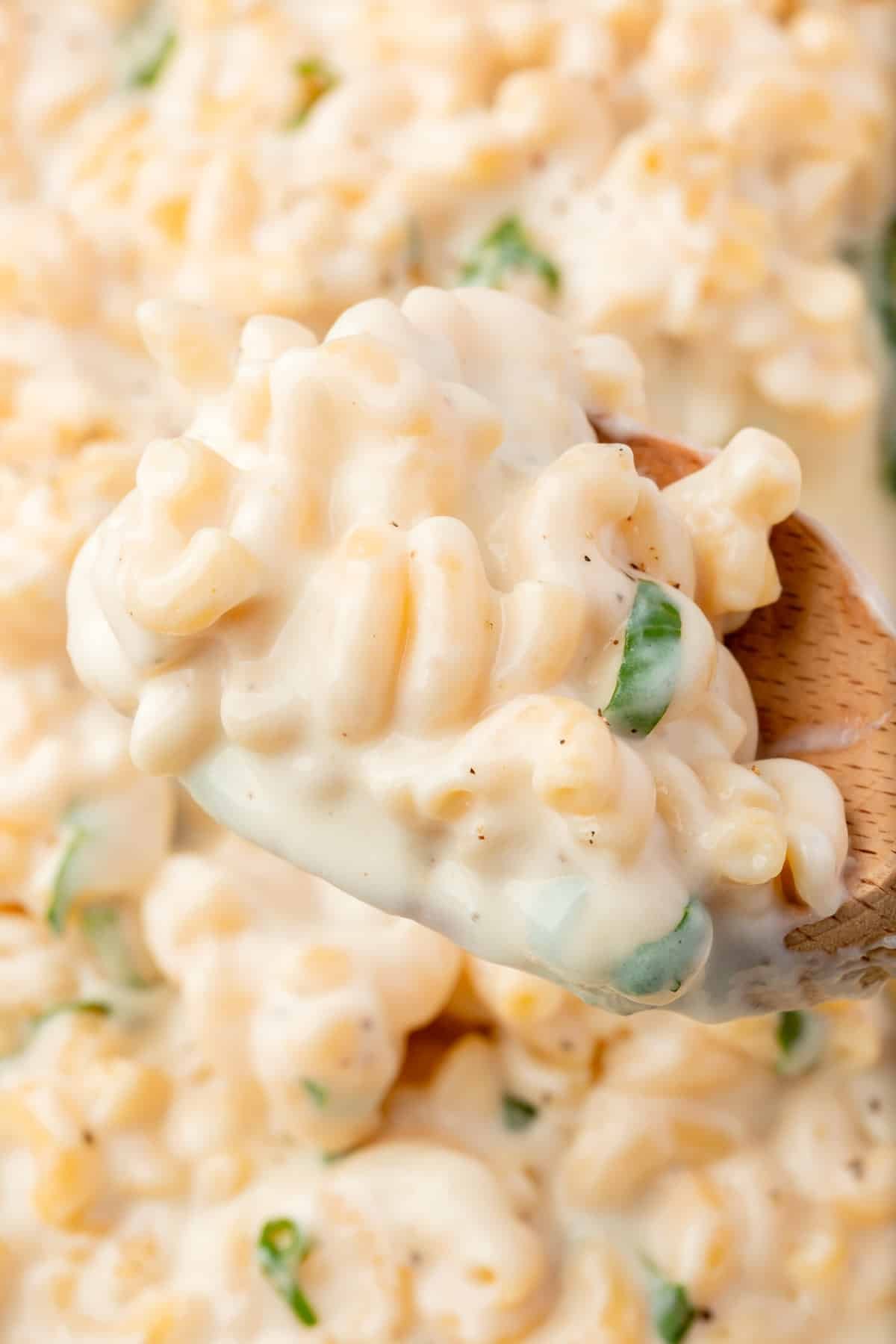 A closeup of a wooden spoon with a big scoop of mozzarella mac and cheese over a large skillet of mac and cheese.