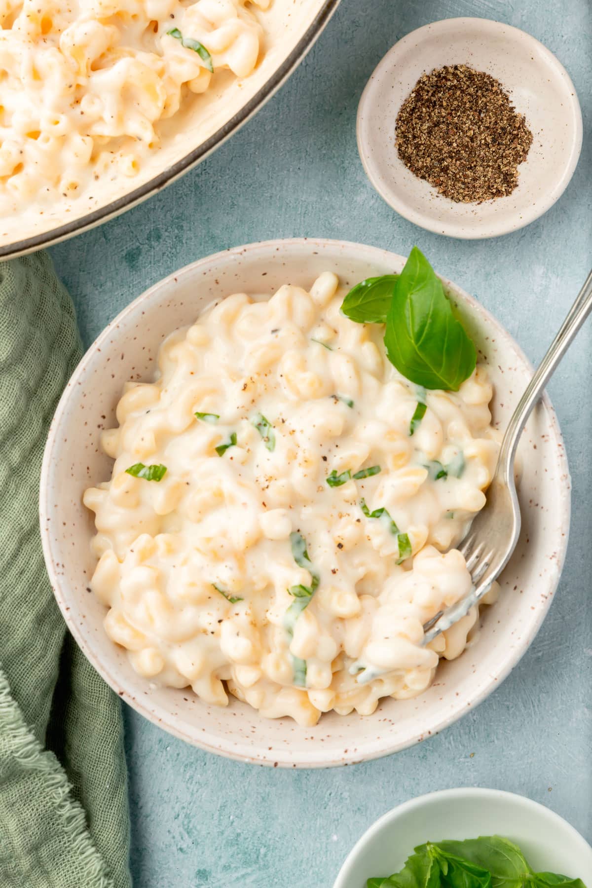 A bowl of mozzarella mac and cheese topped with basil with a small bowl of ground black pepper to the side.
