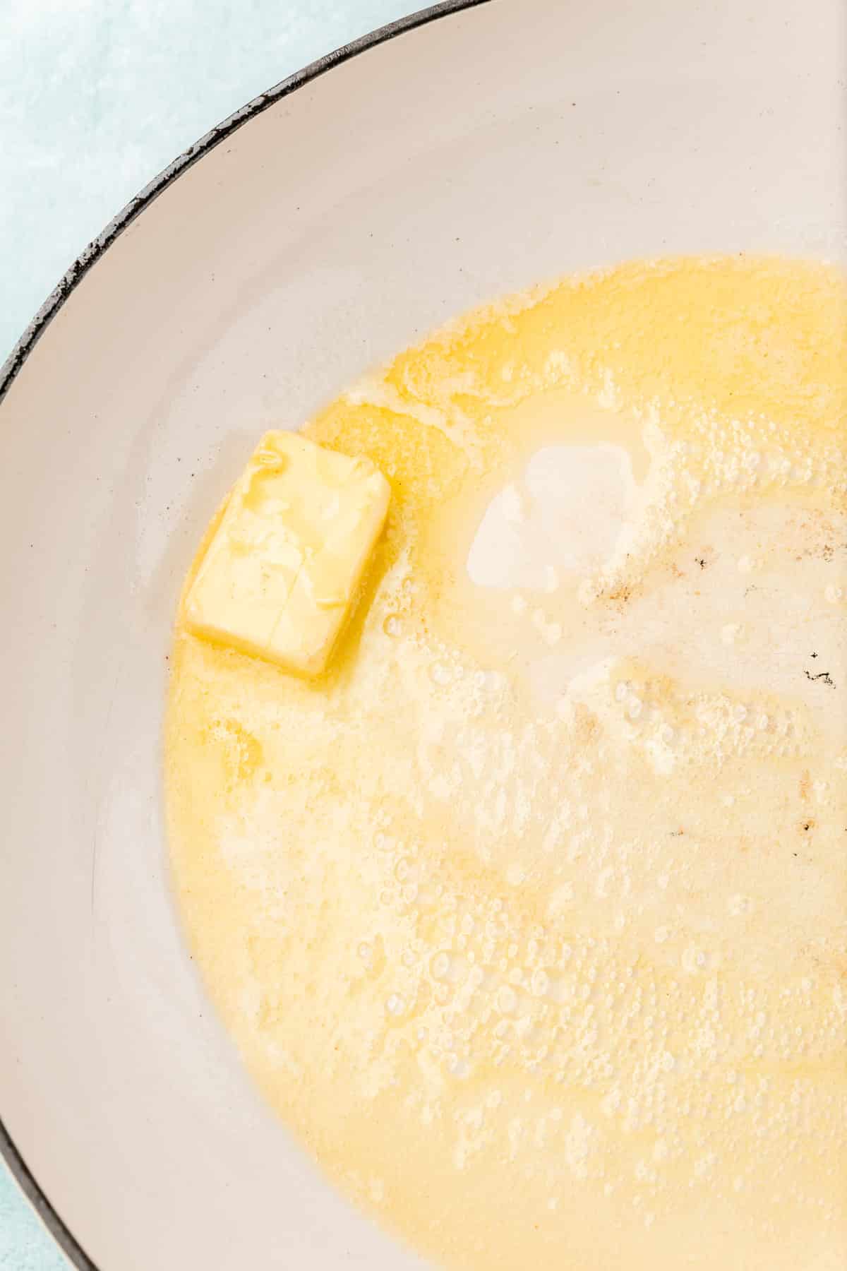 A knob of butter melting in a large white skillet.