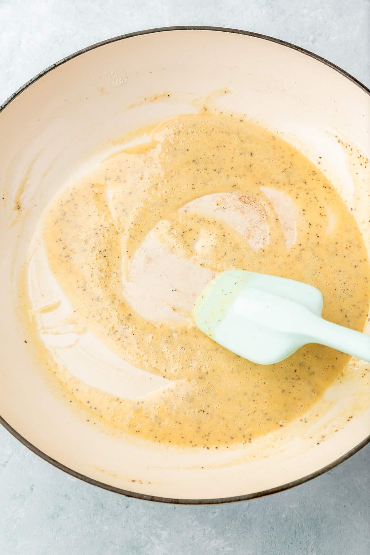 A gluten-free roux being stirred together by a blue spatula in a white braiser pan.