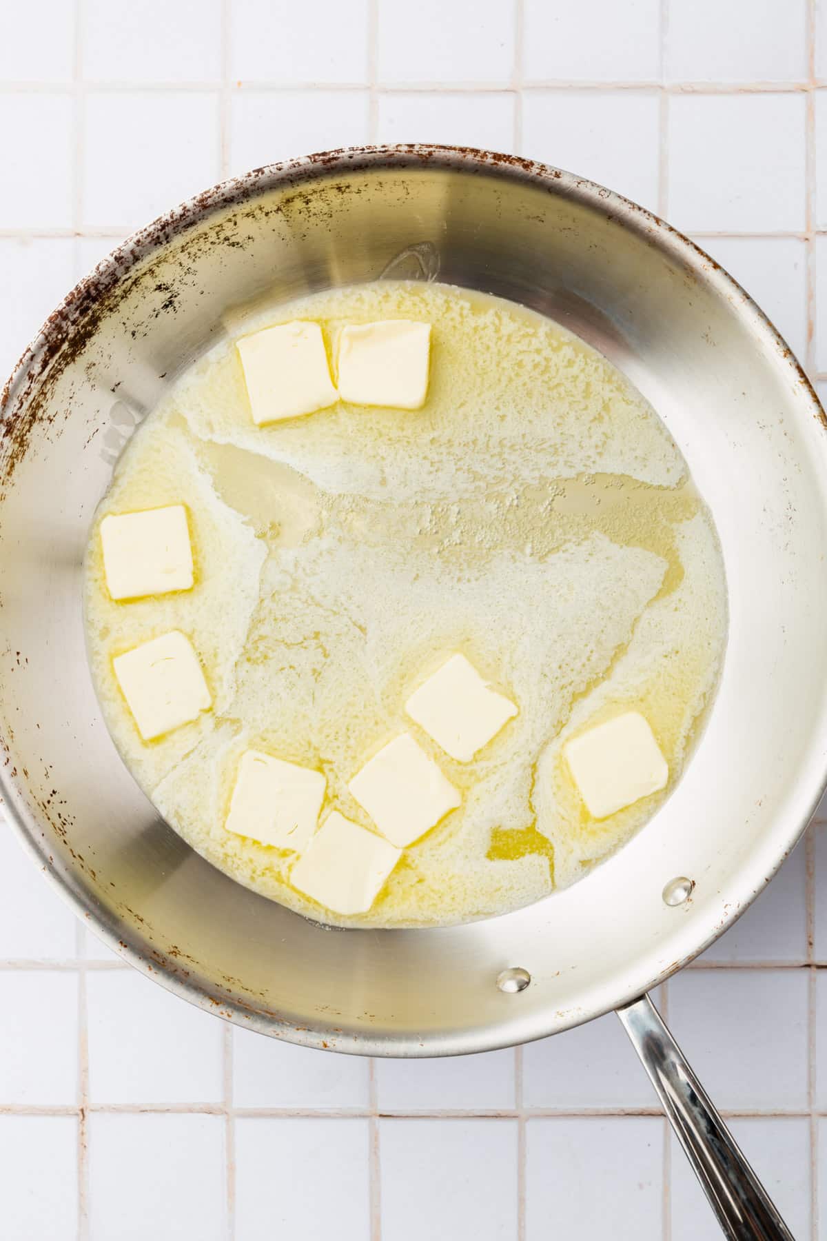 A stainless steel skillet with pats of butter that are beginning to melt.