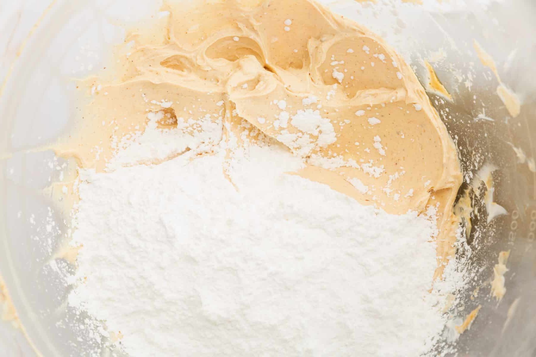 A glass mixing bowl with browned butter and powdered sugar before mixing together.
