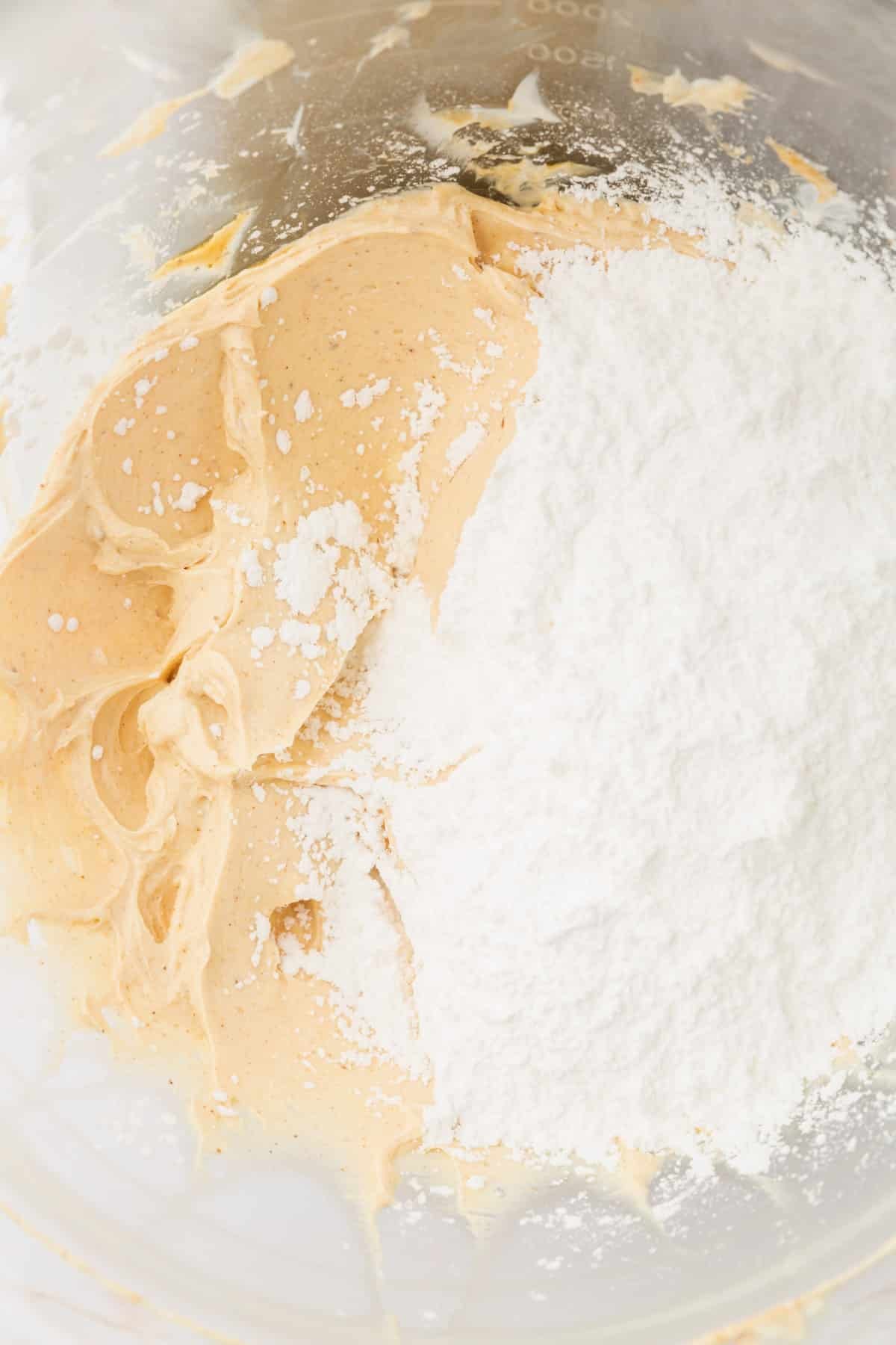 A glass mixing bowl with browned butter and powdered sugar before mixing together.