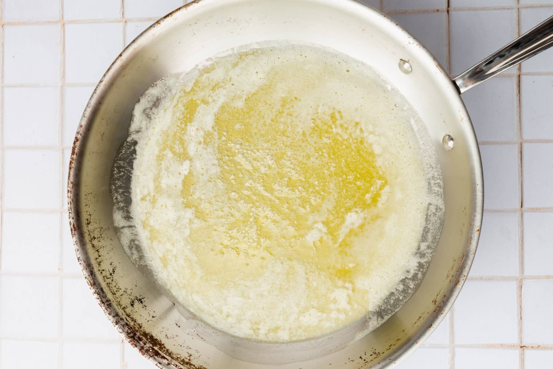 A stainless steel skillet with melted butter that is beginning to foam up.