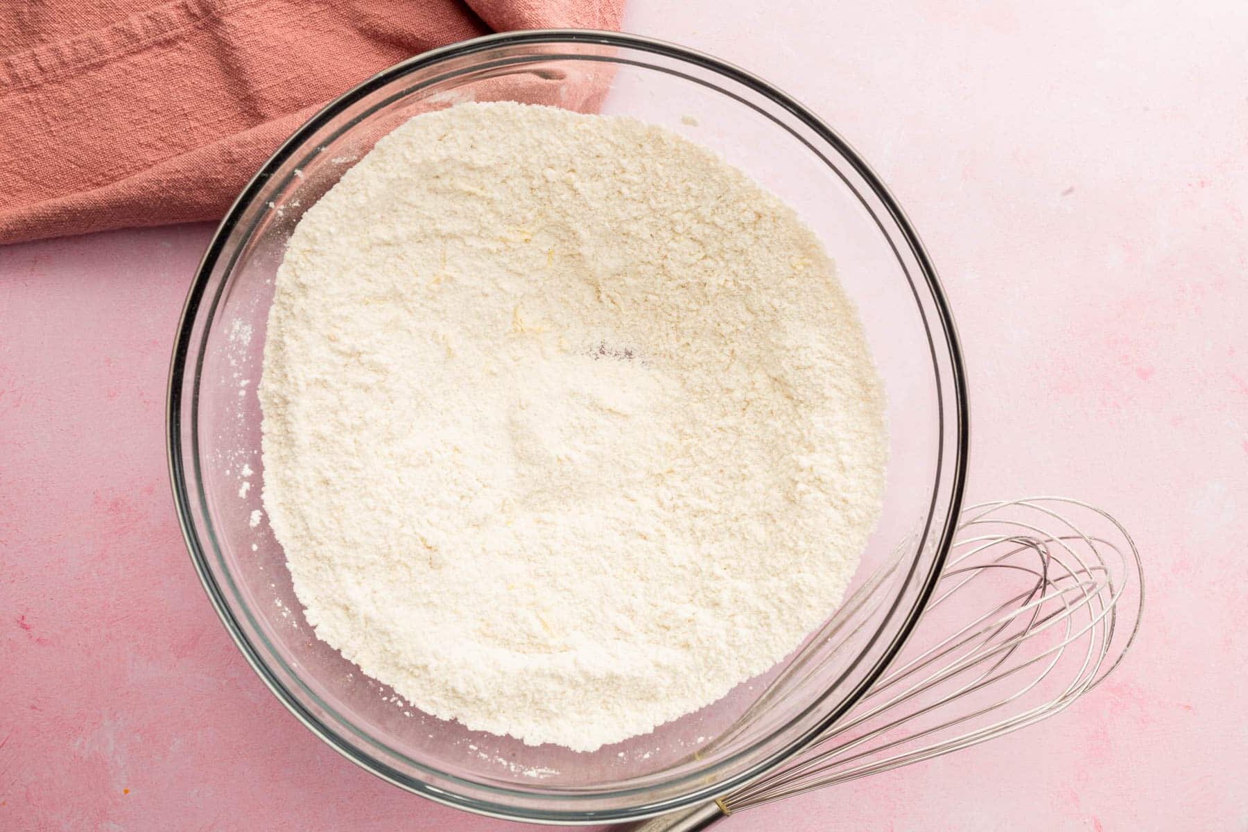 A glass mixing bowl with a gluten-free flour mixture and a whisk.
