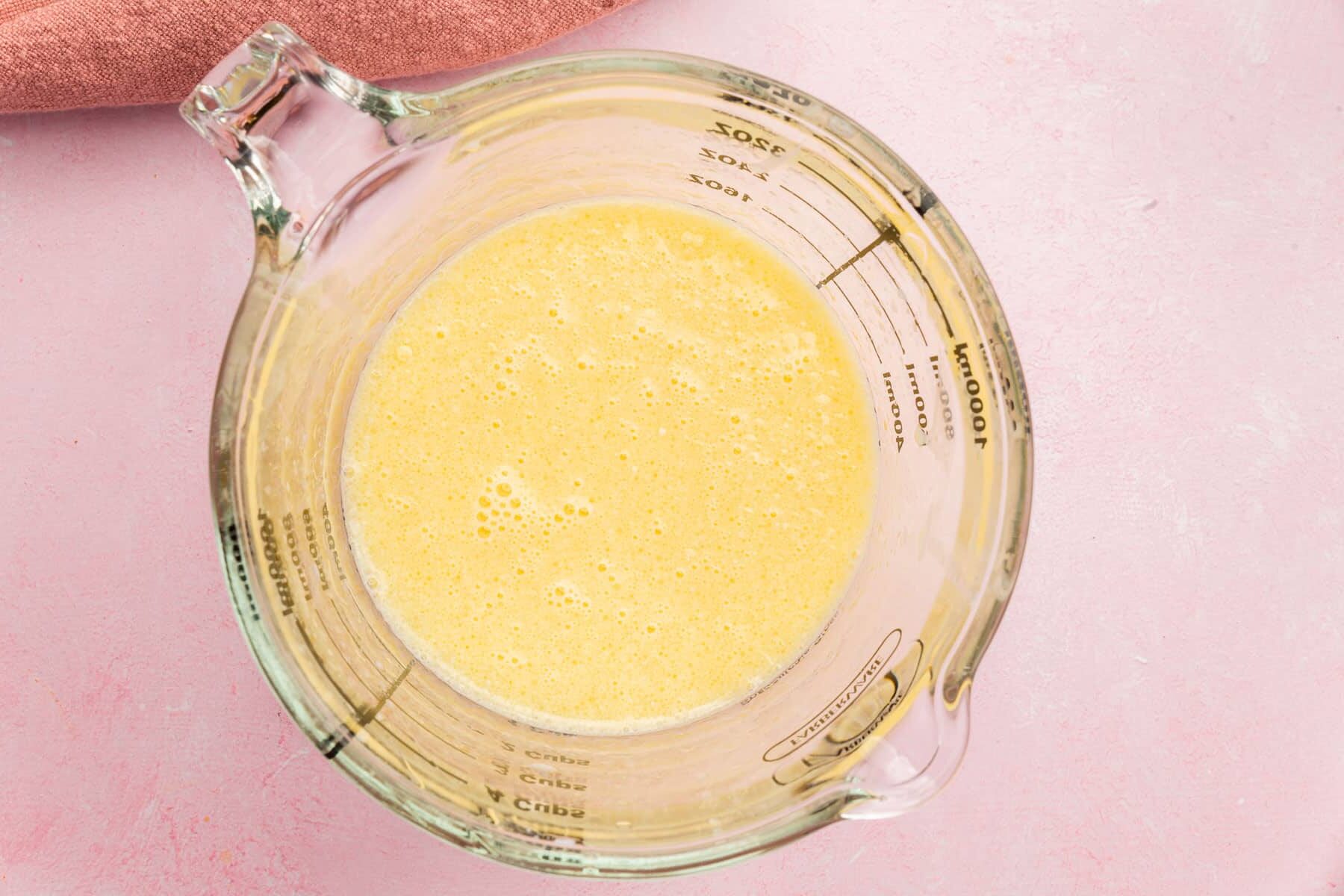A glass measuring cup with a yellow mixture made of eggs, sugar and oil.