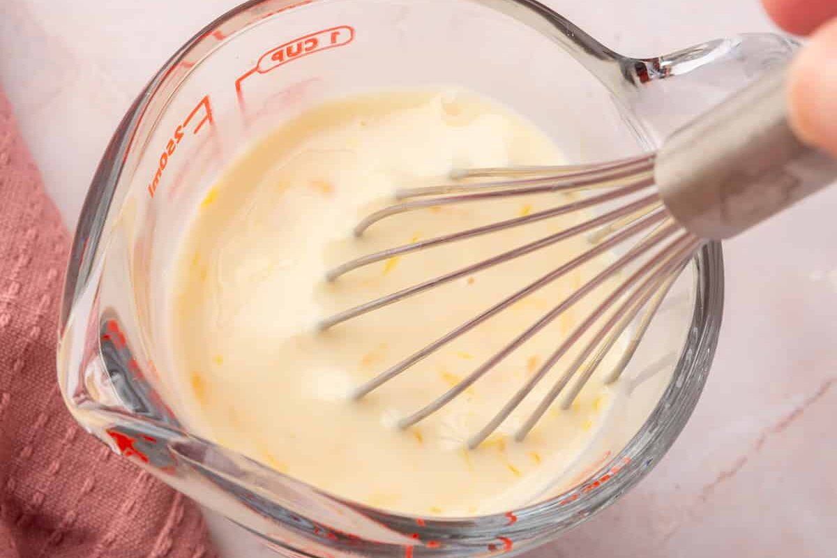 A whisk mixing together a buttermilk and egg mixture in a glass measuring cup.