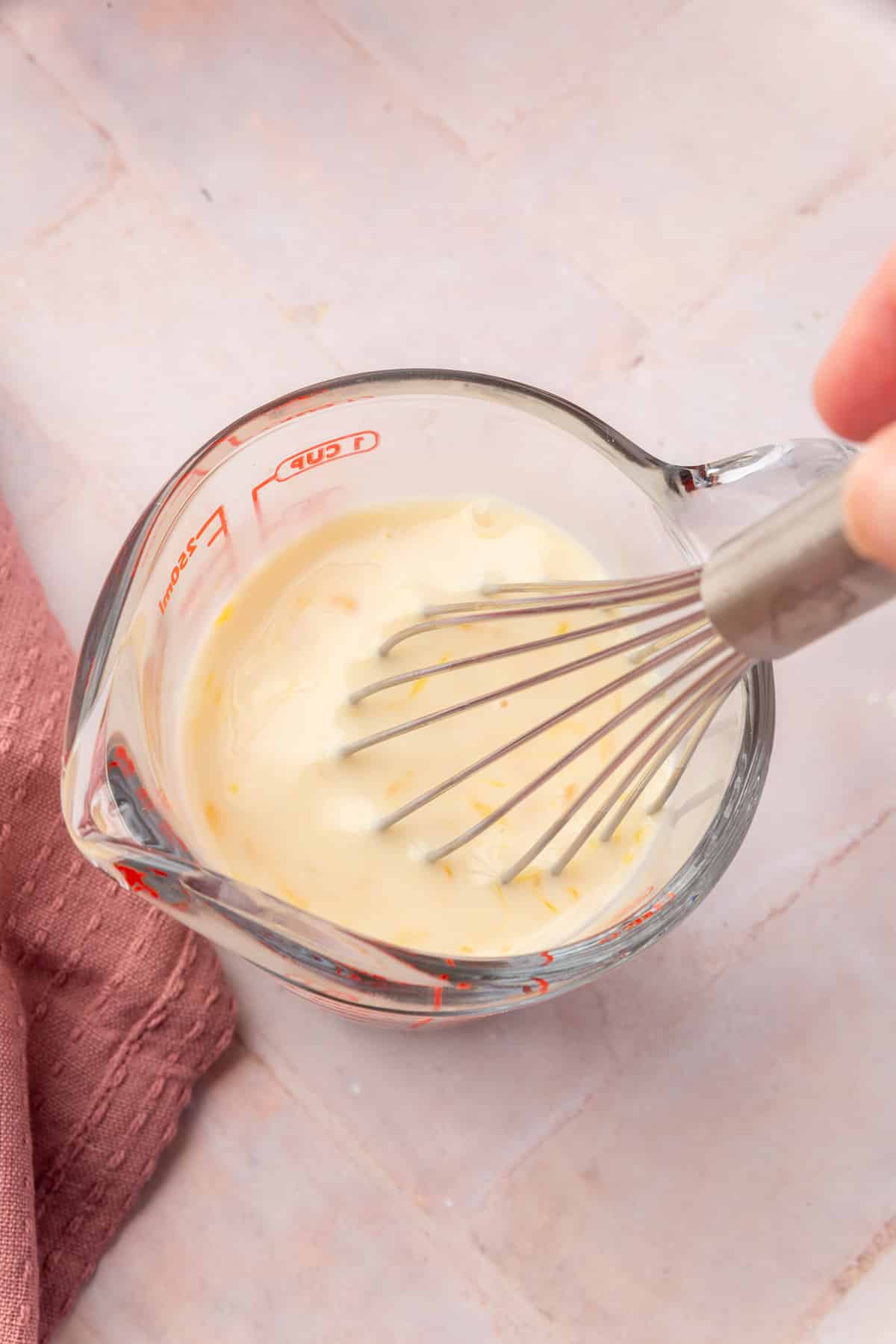 A whisk mixing together a buttermilk and egg mixture in a glass measuring cup.