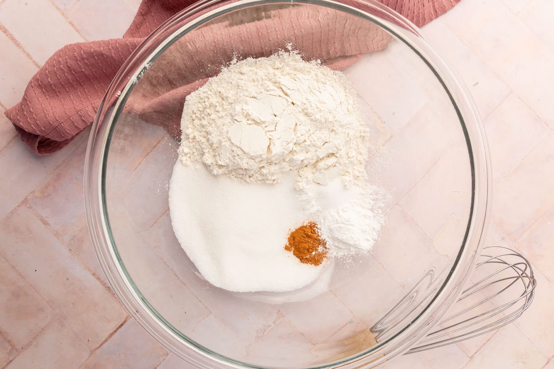 A glass mixing bowl with gluten-free flour, sugar, cinnamon, salt, and baking powder before mixing together.