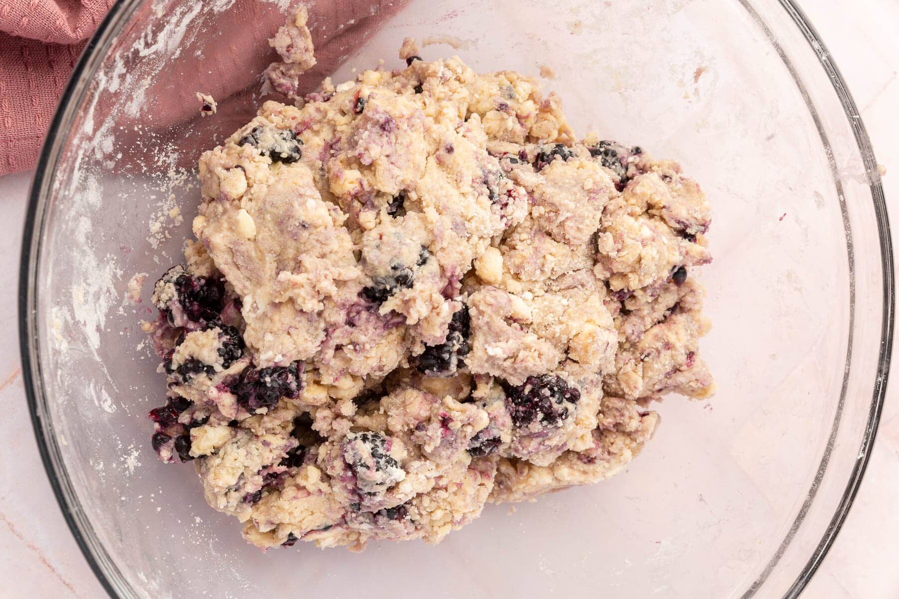 A glass mixing bowl filled with gluten-free blackberry scone dough.