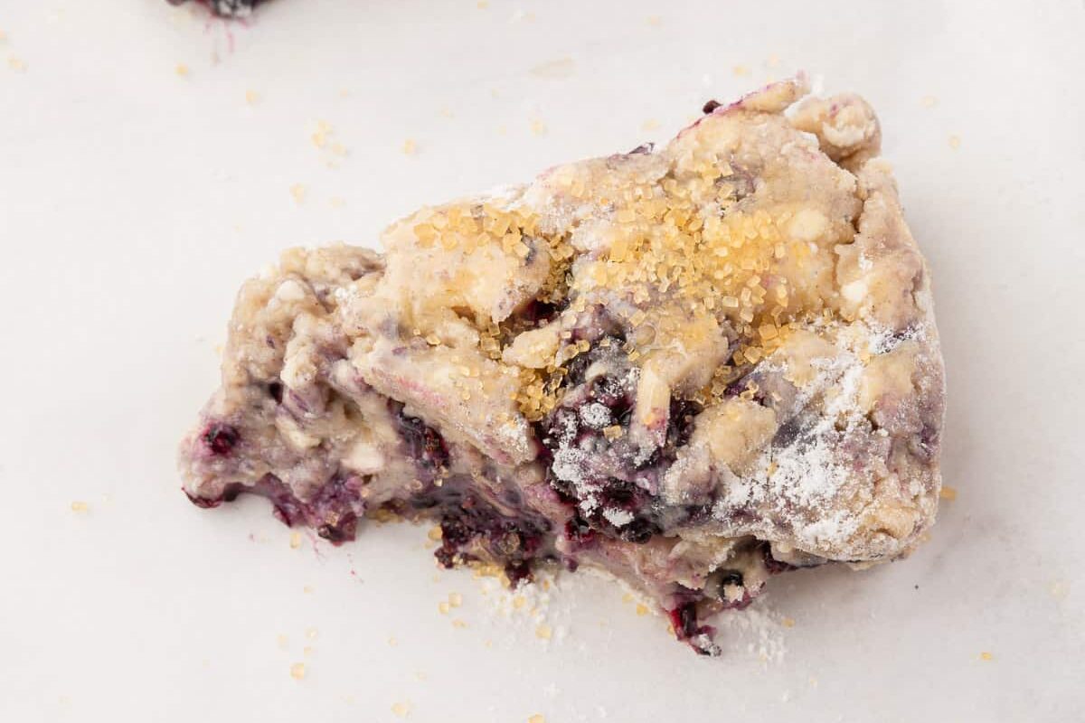 A close up of wedges of gluten free blackberry scone dough on a parchment paper lined baking sheet.