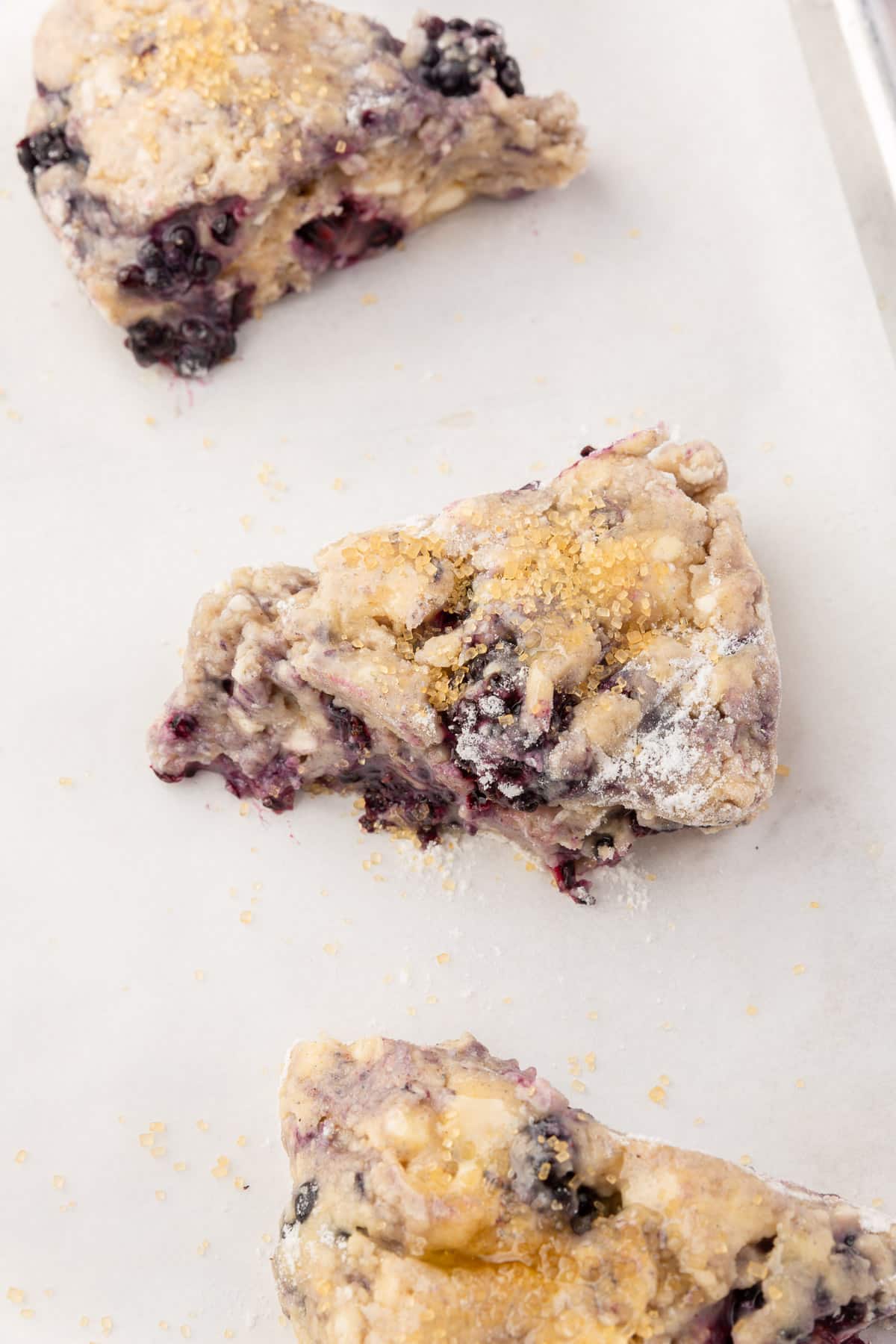 A close up of wedges of gluten free blackberry scone dough on a parchment paper lined baking sheet.