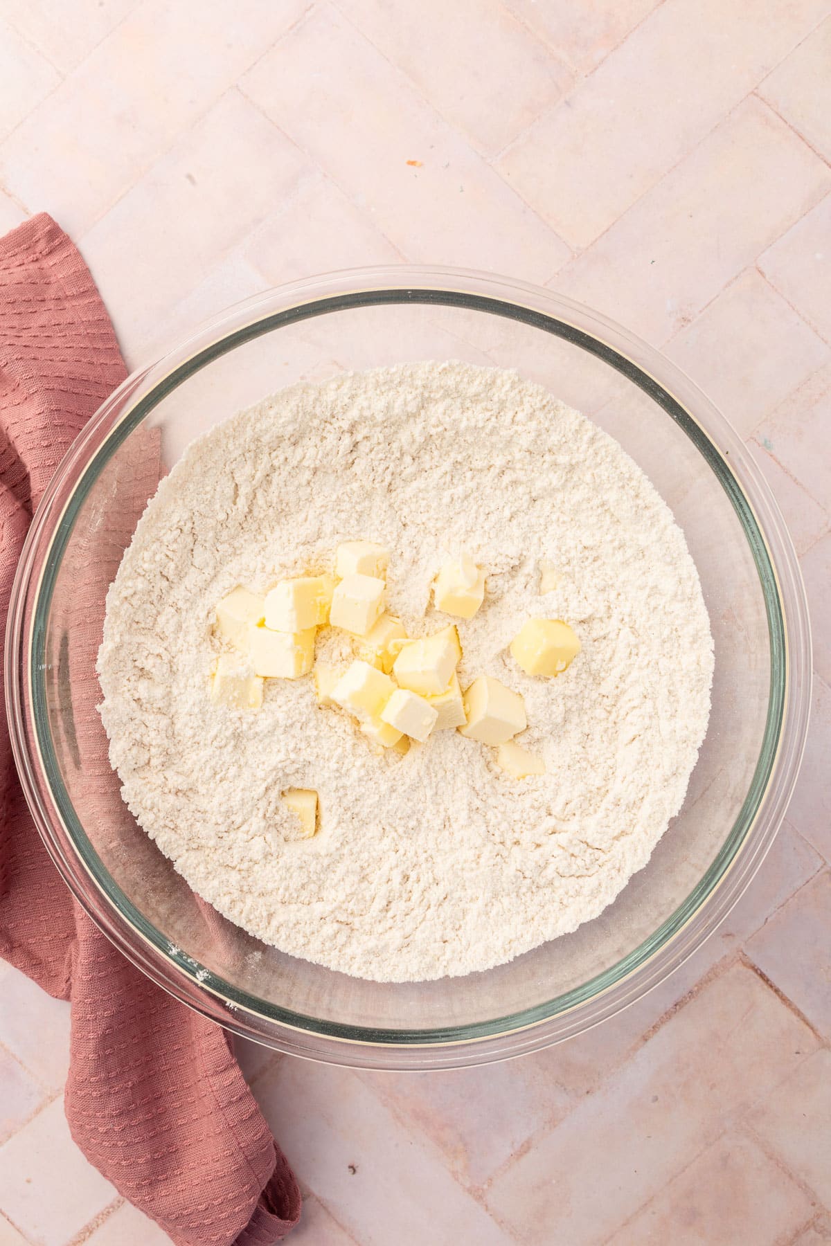 An overhead view of a glass mixing bowl with a gluten-free flour blend topped with cubes of cold unsalted butter.