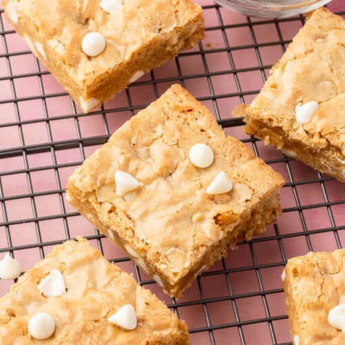 Gluten-free blondie squares cooling on a wire cooling rack with a bowl of white chocolate chips to the side.