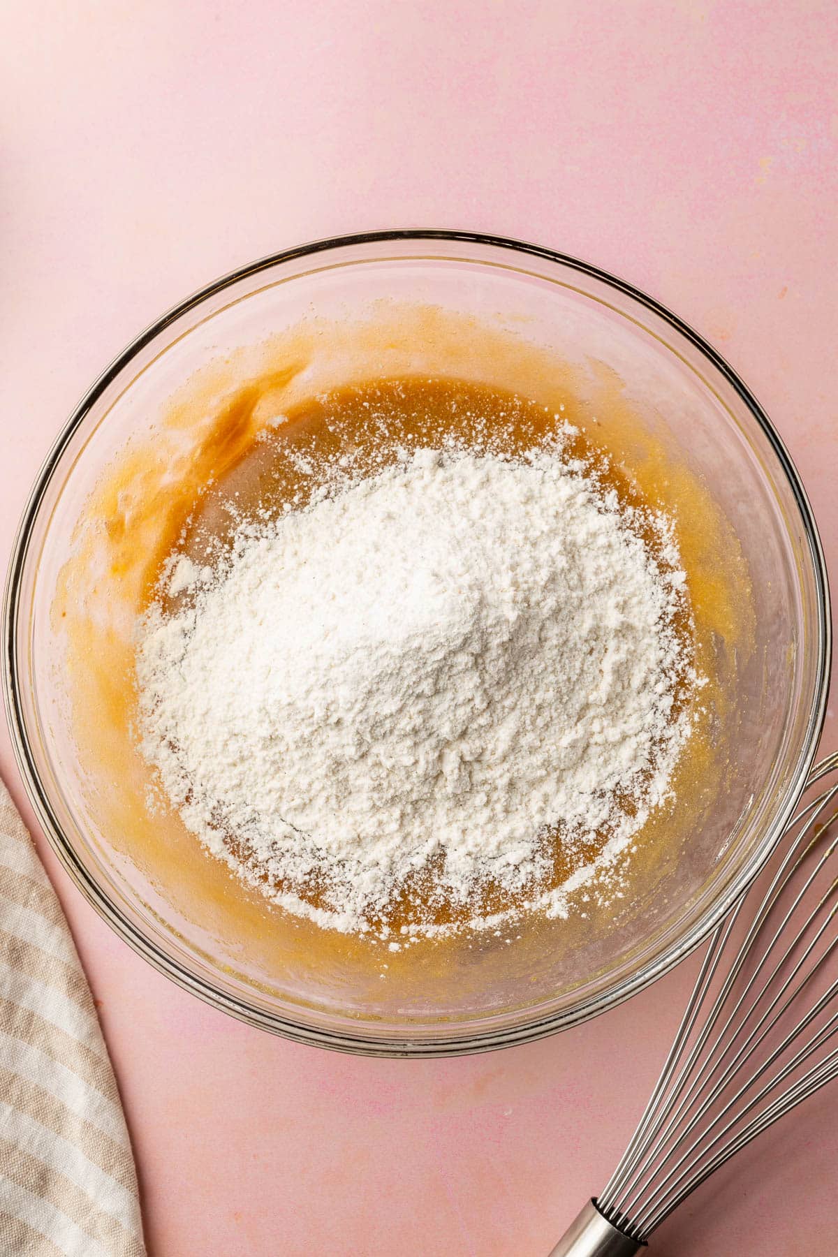 A glass mixing bowl filled with a brown sugar liquid topped with a gluten-free flour blend.