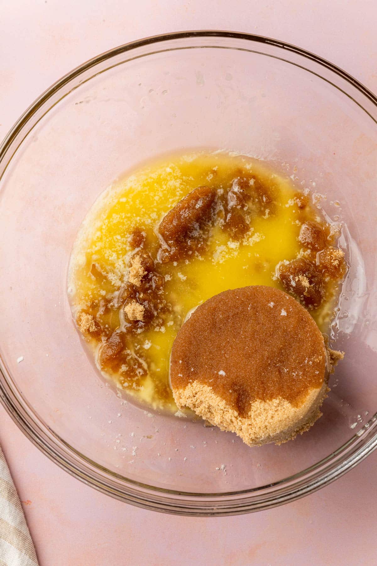 A glass mixing bowl filled with melted butter and a scoop of brown sugar before mixing together.