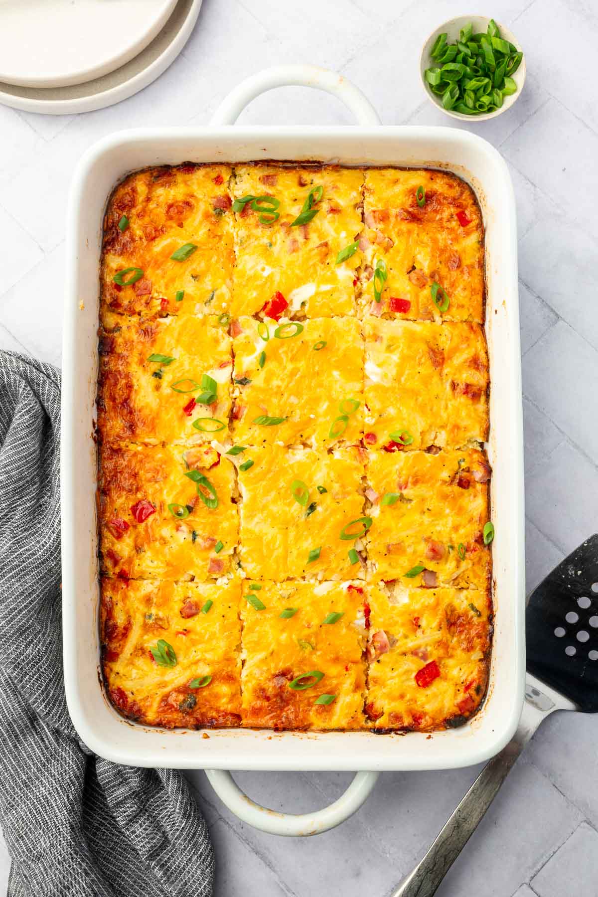 An overhead view of a rectangle casserole dish filled with slices of gluten free ham breakfast casserole topped with green onions.