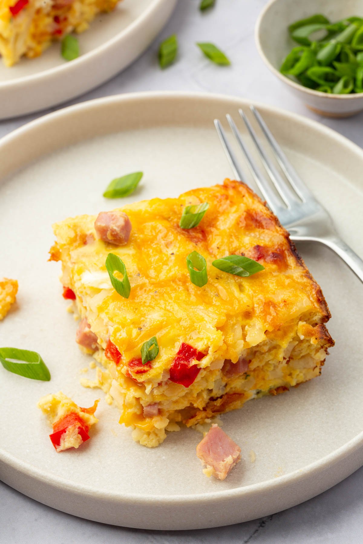 A slice of gluten free hash brown casserole on a plate with a fork.