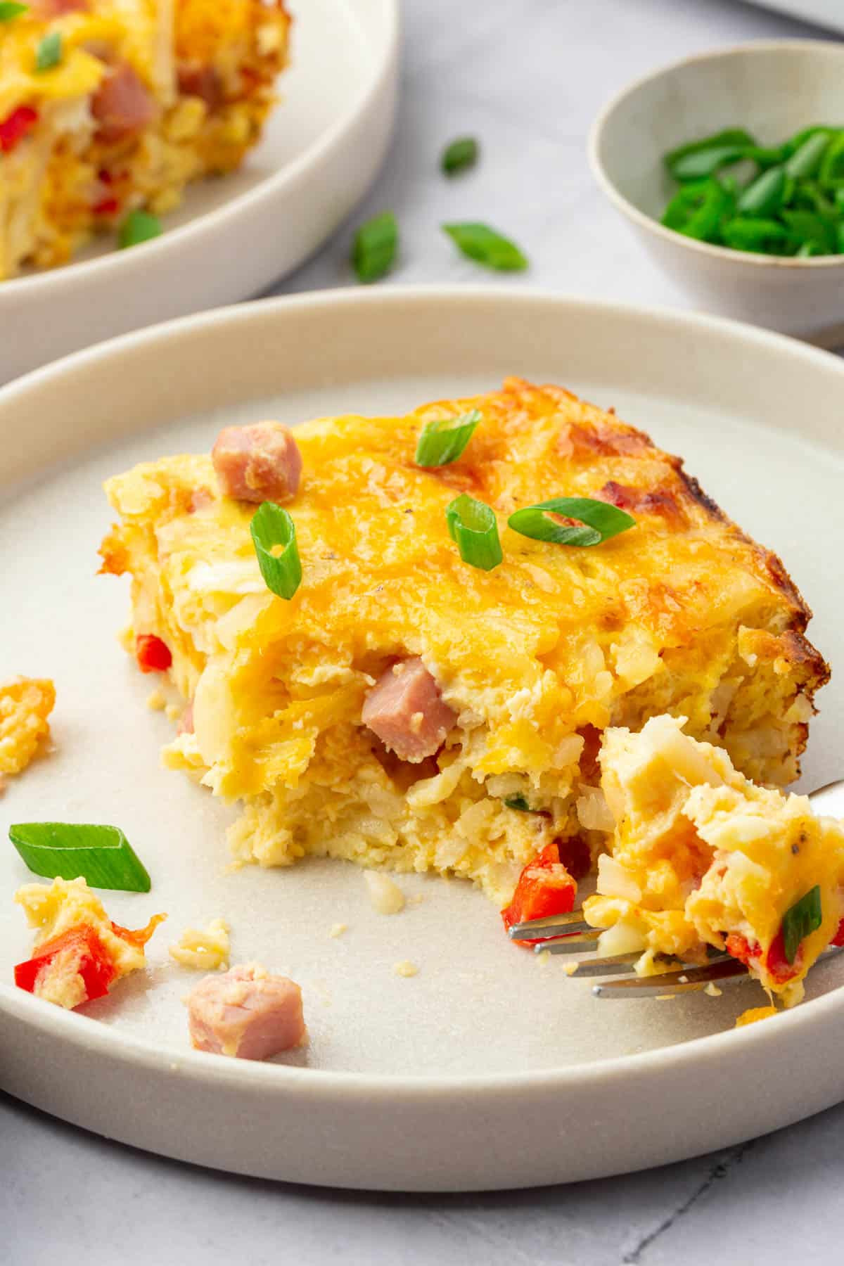 A closeup of a slice of gluten free ham breakfast casserole topped with green onions that has a bite removed from it.