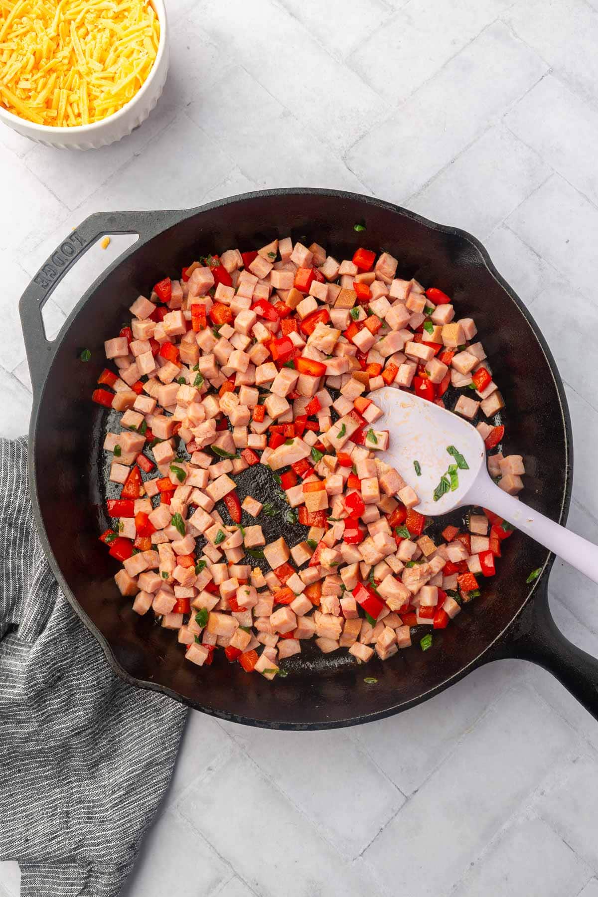 A cast iron skillet with sautéed cubed ham and red bell pepper with a spatula in it.