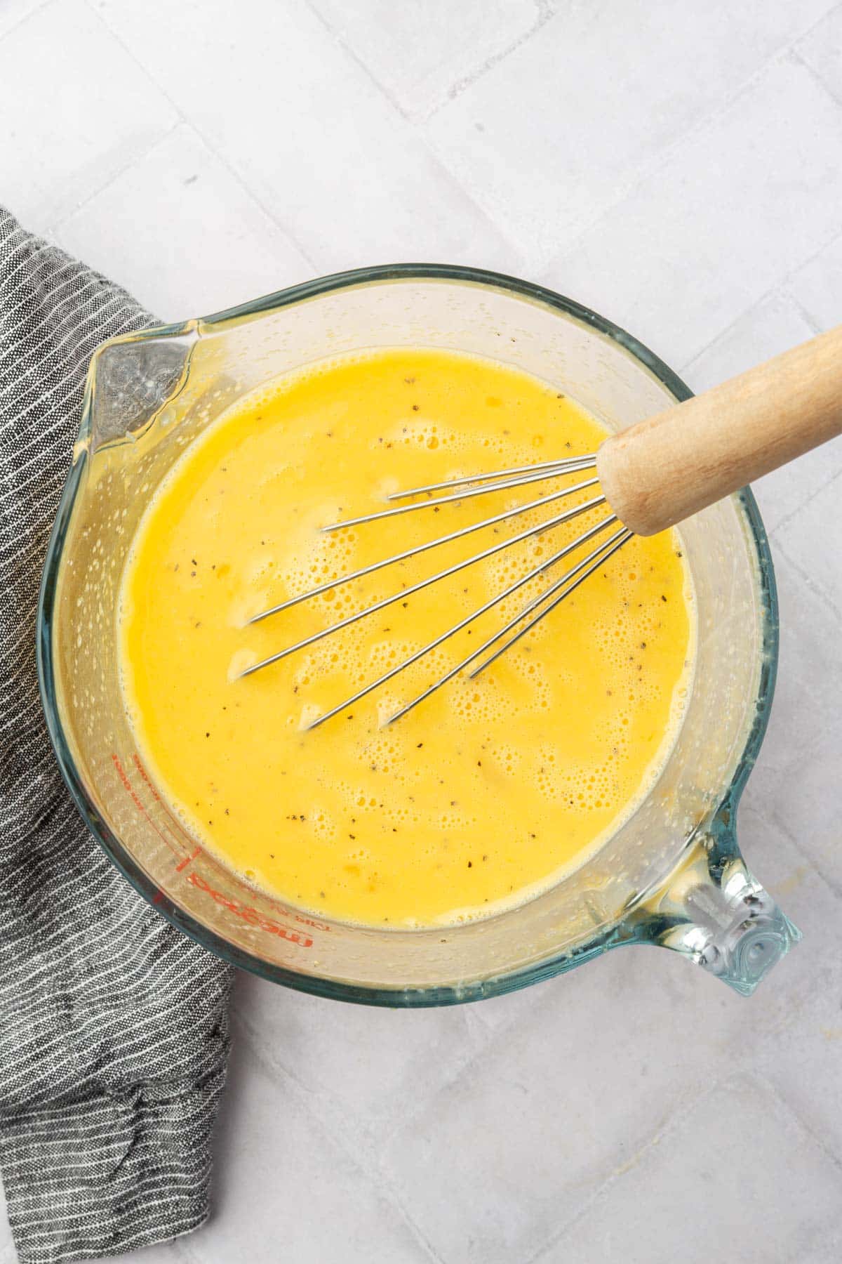 A large measuring cup with a egg, milk and black pepper mixture with a whisk in it.