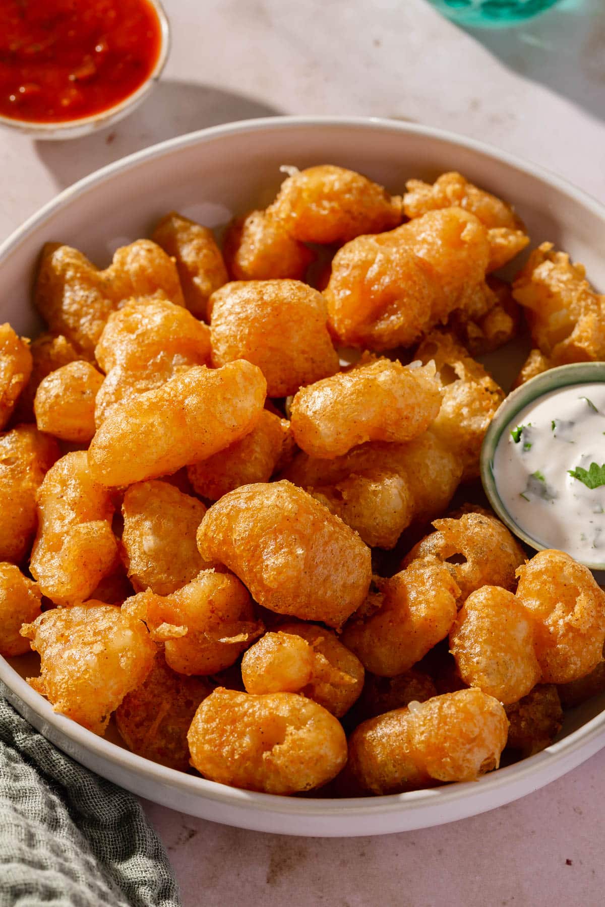 A low serving bowl of gluten-free fried cheese curds with a side of cilantro ranch dressing and marinara sauce.