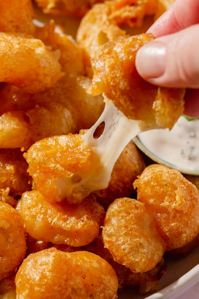 A hand pulling apart a gluten-free cheese curd to see the cheesy center.