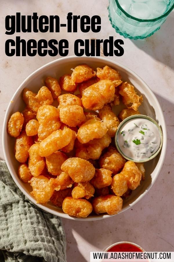 An overhead view of a bowl of gluten-free cheese curds that have been deep fried with a small ramekin of ranch dressing and another ramekin of marinara sauce on the side.