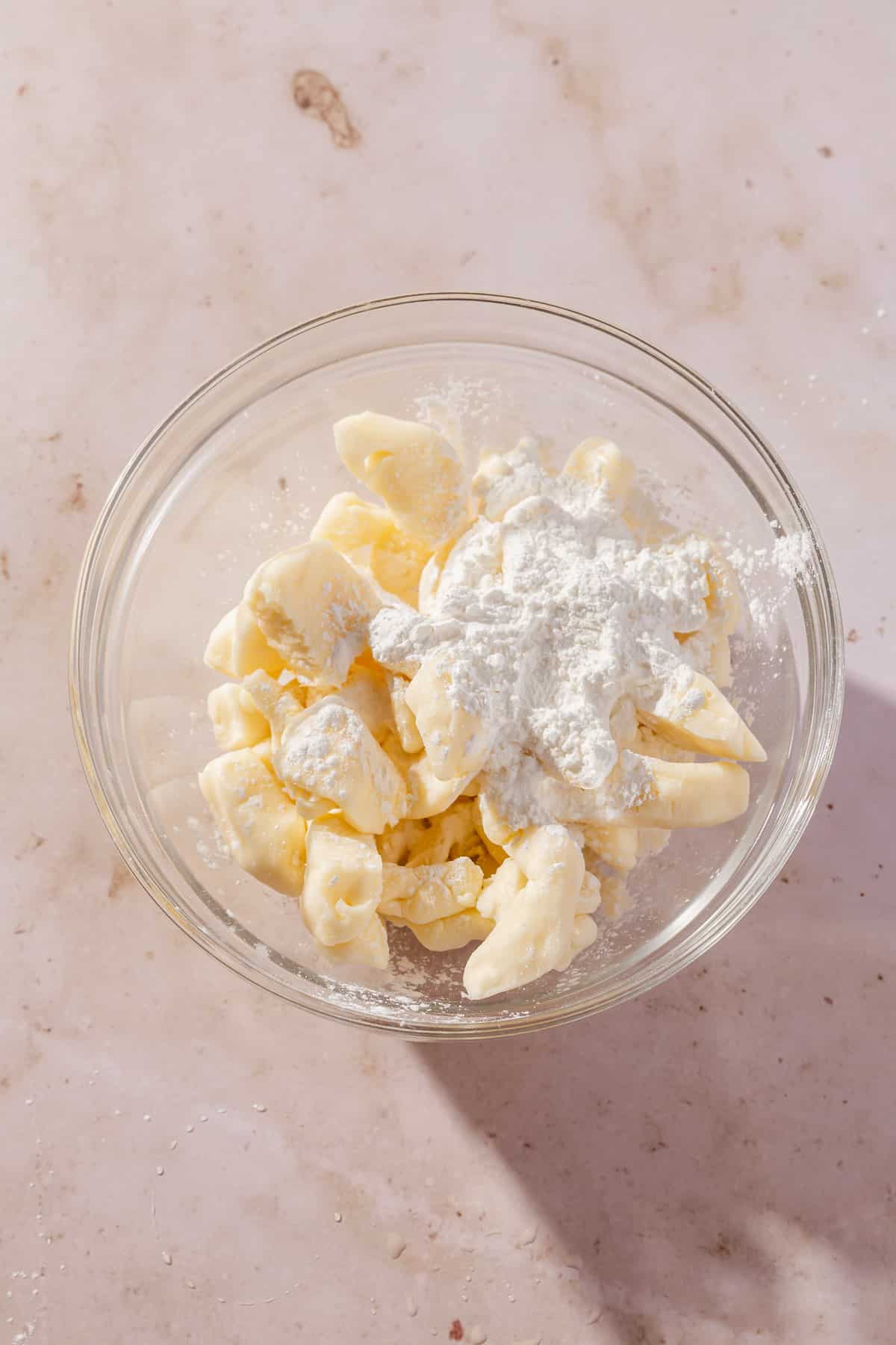 A glass mixing bowl with a pile of white cheddar cheese curds topped with cornstarch before tossing together.
