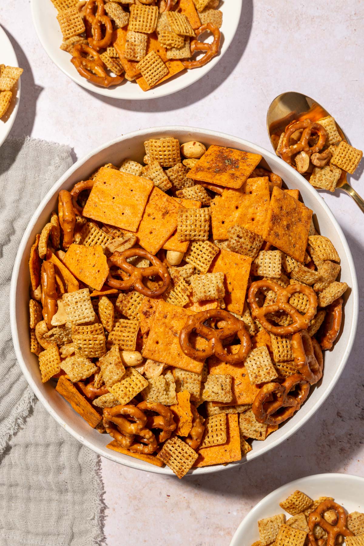 A large serving bowl with gluten-free chex mix in it with appetizer plates filled with snack mix to the side and a serving spoon.