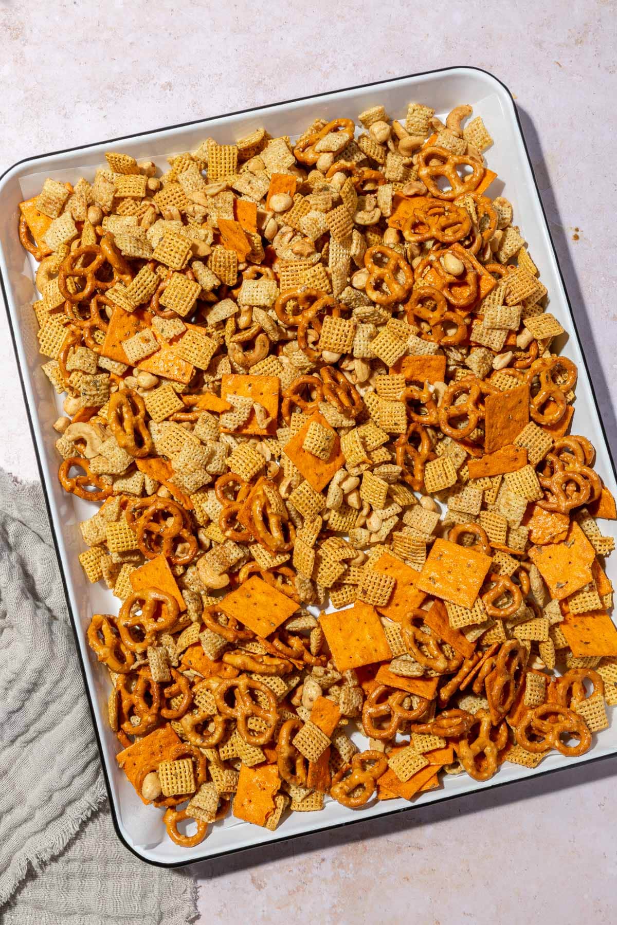 A white sheet pan with gluten-free chex mix on it after baking in the oven.
