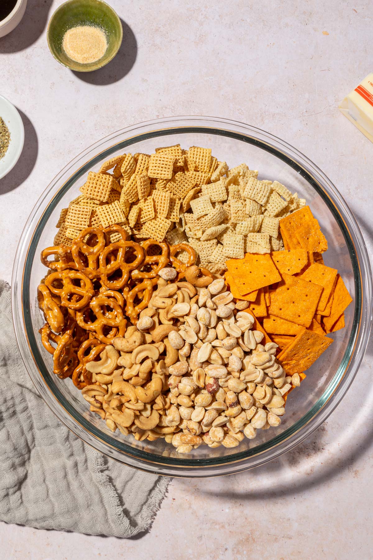 A glass mixing bowl with gluten-free pretzels, rice chex cereal, corn chex cereal, gluten-free cheese crackers, cashews and peanuts in it.